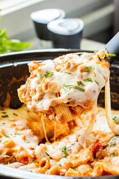 a spoon full of lasagna being lifted from a casserole dish with meat and cheese