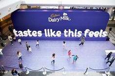 many people are walking around in front of a dairy milk sign that says tastes like this feeds