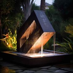 a water fountain in the shape of a house is lit up at night with lights