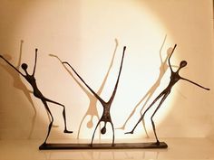 three metal sculptures are standing on a white surface in front of a light that is reflecting off the wall