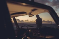 a man standing in front of a car next to the ocean at sunset or dawn