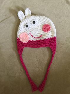 a crocheted hat with a smiling face on the front and side, made to look like a cow