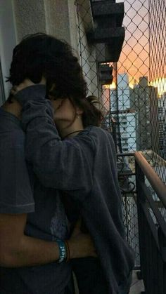 a man and woman hugging on the balcony of a building at sunset with city lights in the background