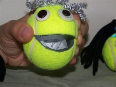 a person holding a tennis ball with a face drawn on it's side and another stuffed animal in the background