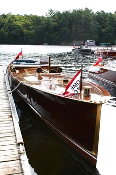 several boats are docked on the water near a dock with trees in the backgroud