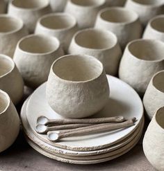 a table topped with lots of white bowls and saucers next to wooden spoons