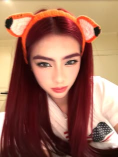 a woman with long red hair wearing an orange knitted fox ears headband and looking at the camera