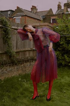 a woman in a red and blue dress is leaning against a fence with her hands behind her head