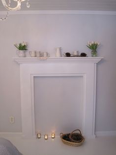 a white fireplace with candles and flowers on it in a room that is painted white