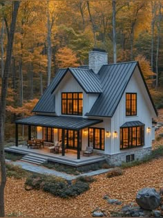 a house in the woods surrounded by trees and leaves with lights on it's windows