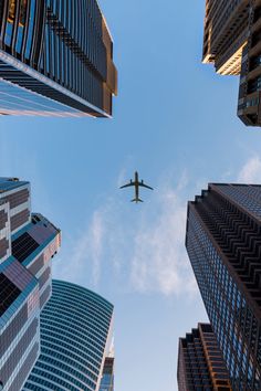 an airplane is flying in the sky between some tall buildings