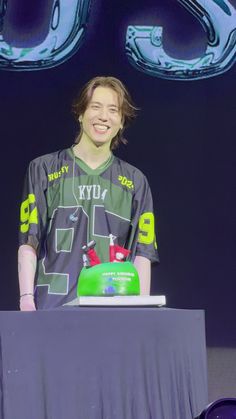 a young man standing at a table with a cake in front of him on stage