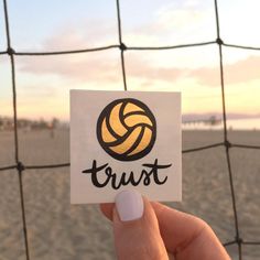 a person holding up a sticker with the word trust on it in front of a beach