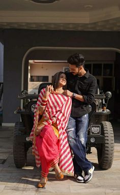 a man standing next to a woman in a red and white sari on top of a jeep