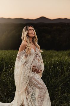 a woman standing in a field wearing a white lace dress and holding her hands on her hips