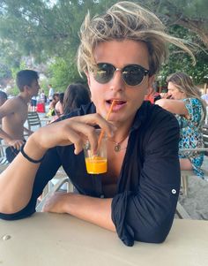 a young man with sunglasses on drinking orange juice at an outdoor table in the sun