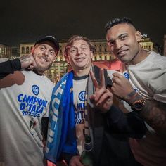 three men standing next to each other in front of a building at night with one holding up his peace sign