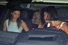 two women sitting in the back of a car talking to each other while another woman looks on