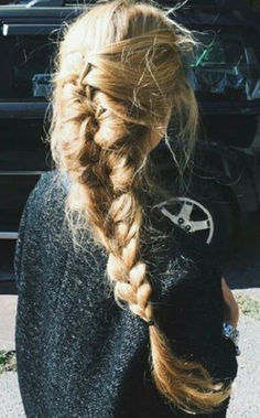 a woman with long blonde hair in a fishtail braid is standing on the sidewalk