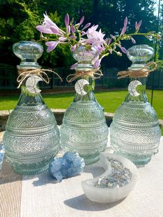 three glass vases sitting on top of a table next to some rocks and flowers