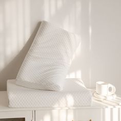 a white bed with two pillows on top of it and a cup next to it