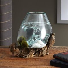 a glass vase filled with water sitting on top of a wooden table next to a book