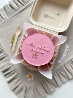 a pink cake with a crown on it sitting next to a fork, spoon and cup