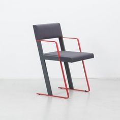 a grey chair with red metal frame and arm rests on a white floor in front of a white wall