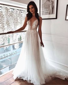 a woman in a white wedding dress standing by a window with her hand on the rail