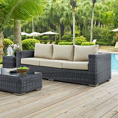 a couch and table on a wooden deck next to a swimming pool with palm trees in the background