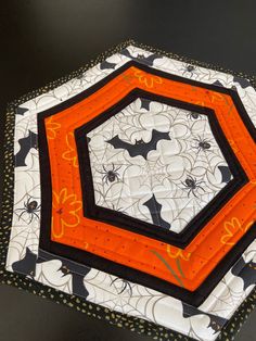 an orange and black hexagonal patchwork piece on a table top with spider webs in the center