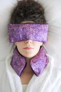 a woman laying in bed with her eyes covered by a purple eye mask that covers her eyes