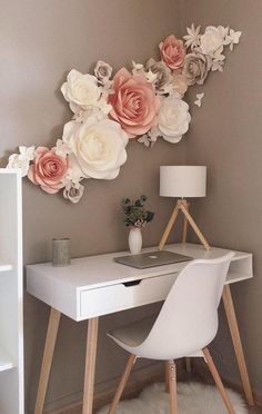 a white desk topped with a laptop computer next to a wall mounted paper flower art