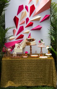 a table topped with cakes and desserts next to a wall covered in paper art