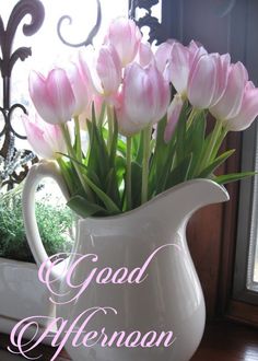 a white pitcher filled with pink tulips on top of a table