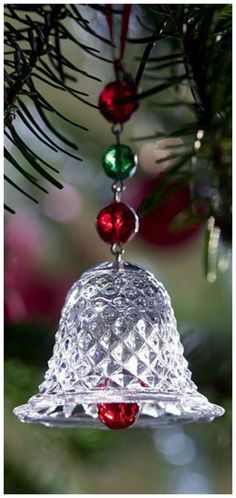 a glass bell ornament hanging from a christmas tree with red and green ornaments