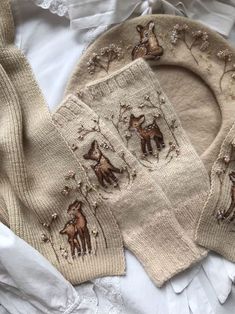 two knitted sweaters with animals on them sitting on top of a white sheet