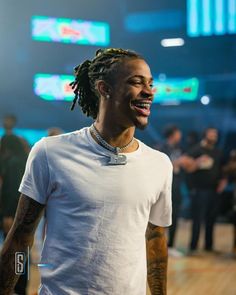 a man with dreadlocks smiles while standing in front of a group of people