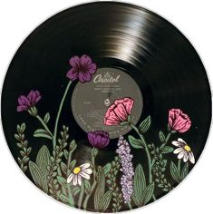 a black record with flowers painted on the front and side, surrounded by greenery