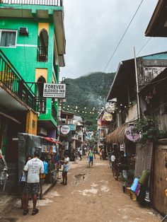 people are walking down the street in front of some shops and buildings with mountains in the background