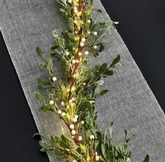 a branch with white flowers and green leaves on a gray table cloth next to a black background