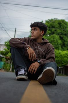 a young man sitting on the side of a road with his hand on his hip