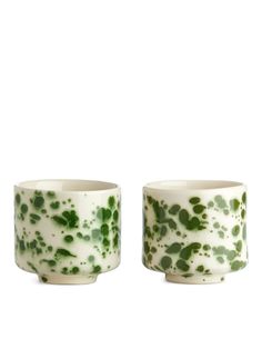 two green and white cups sitting next to each other on a white surface with black dots