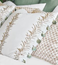 a bed with white and gold pillows on top of each other in front of a green headboard