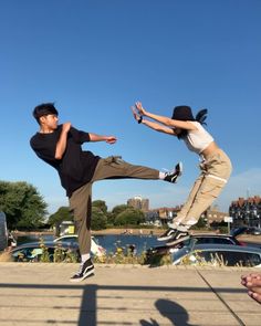 two people doing tricks on their skateboards in the air near some parked cars and water