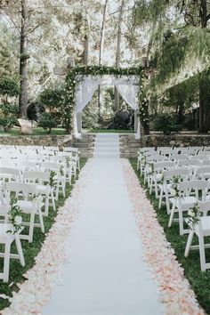 an outdoor ceremony setup with white chairs and flowers on the aisle, surrounded by trees