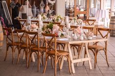 an outdoor dining area with wooden chairs and tables set up for a formal dinner party