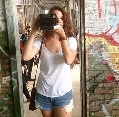 a woman taking a selfie in front of a graffiti covered wall with her camera