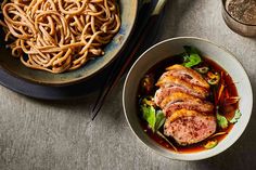 two bowls filled with meat and noodles next to chopsticks on a table top