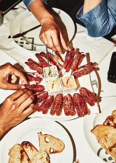 people are cutting up food on plates at a table with breads and crackers